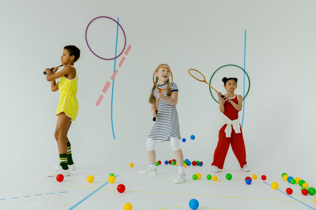 Three diverse children playing tennis indoors with rackets and colorful balls, showcasing fun and diversity.
