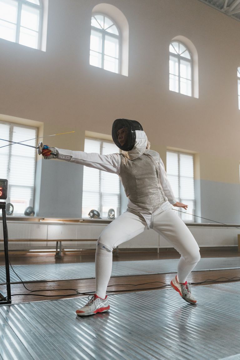 Fencer strikes a dynamic pose in an indoor fencing salle, showcasing skill and precision.