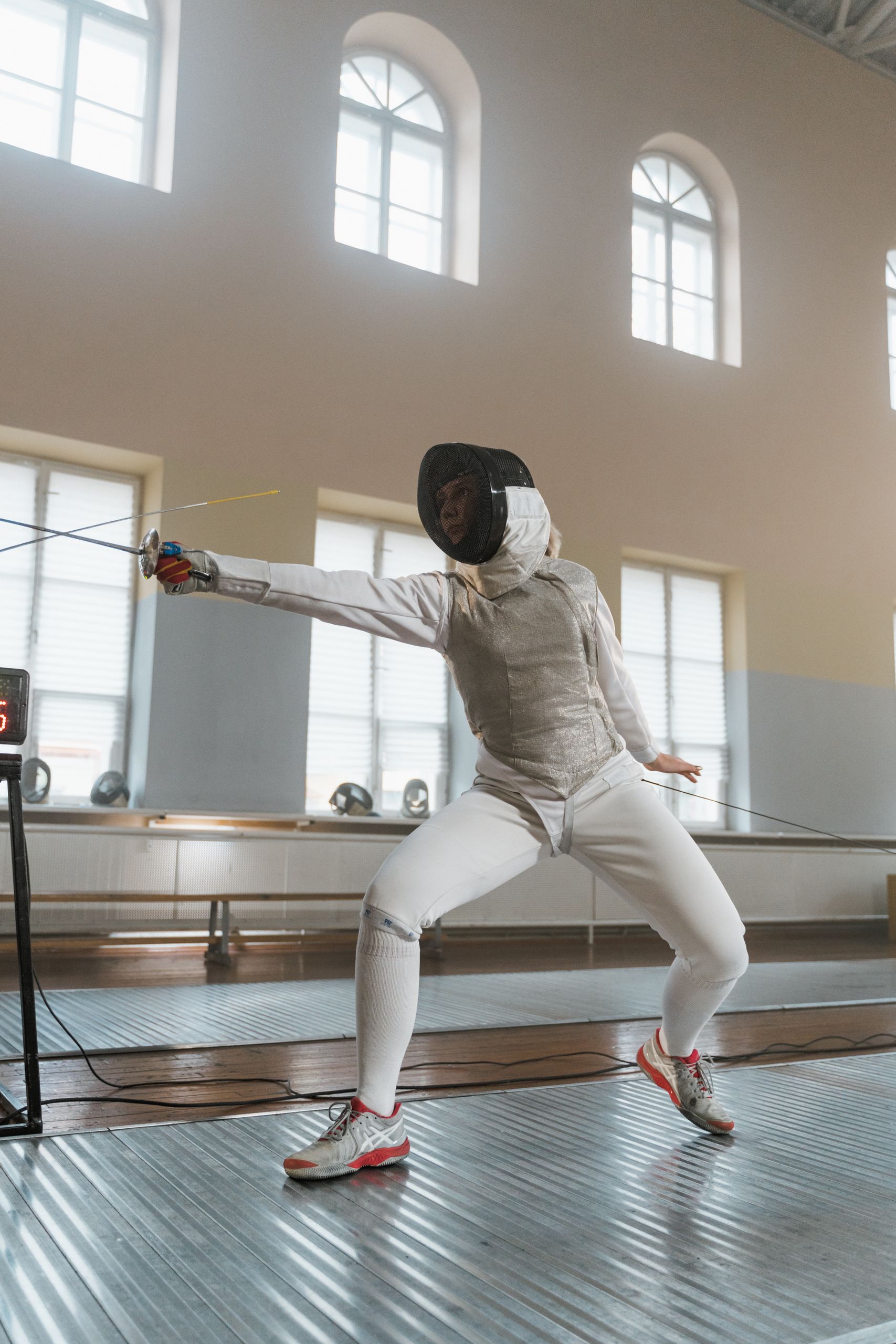 Fencer strikes a dynamic pose in an indoor fencing salle, showcasing skill and precision.